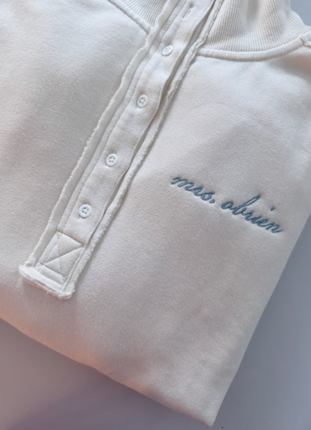 White snap-collar sweatshirt embroidered with the name mrs. obrien in light blue script.