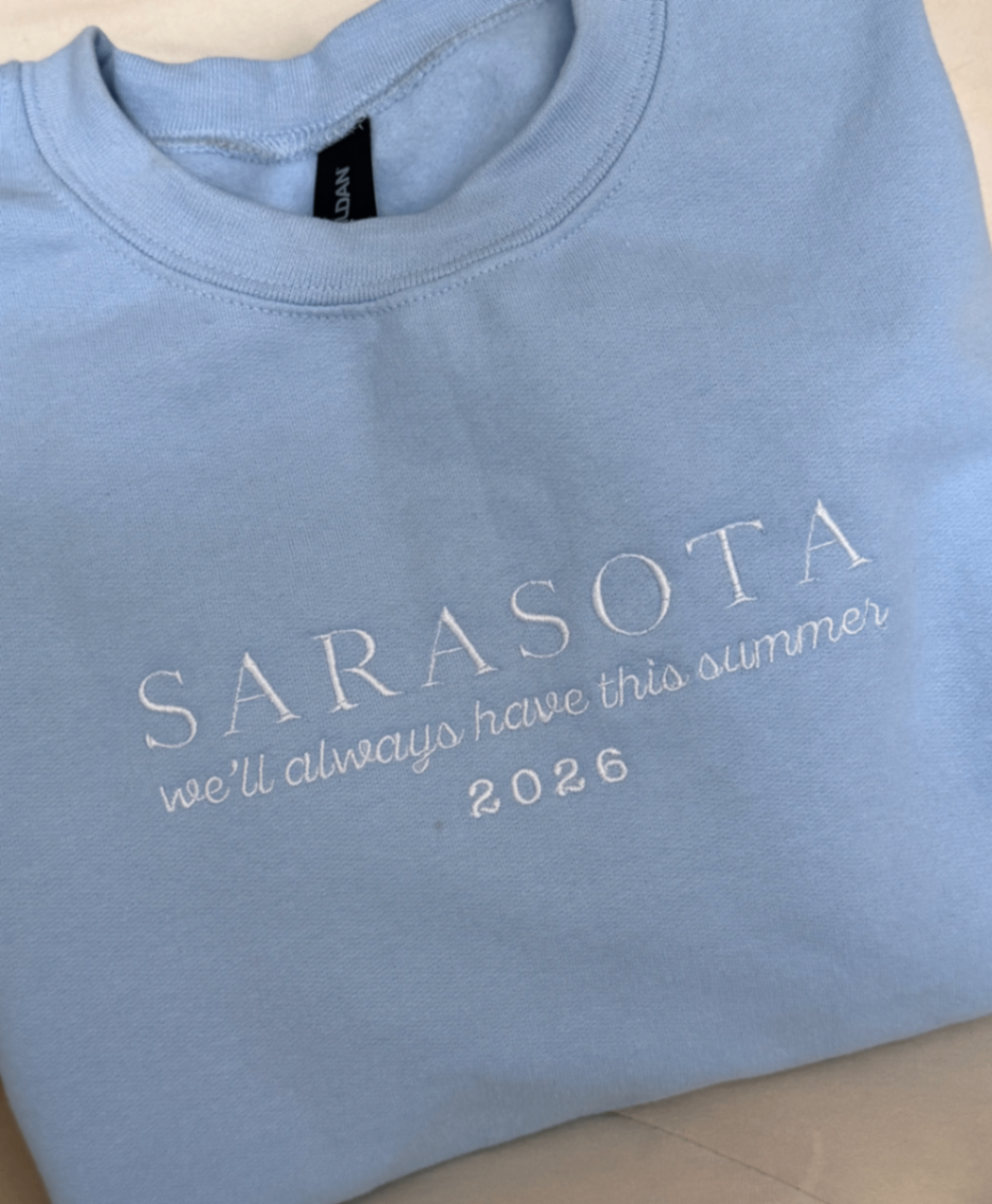 Light blue crewneck sweatshirt embroidered with Sarasota and smaller script text beneath it.