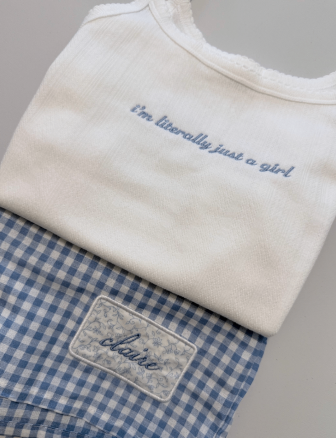 White fabric with blue embroidered phrase paired with blue gingham fabric featuring a custom Claire label patch.