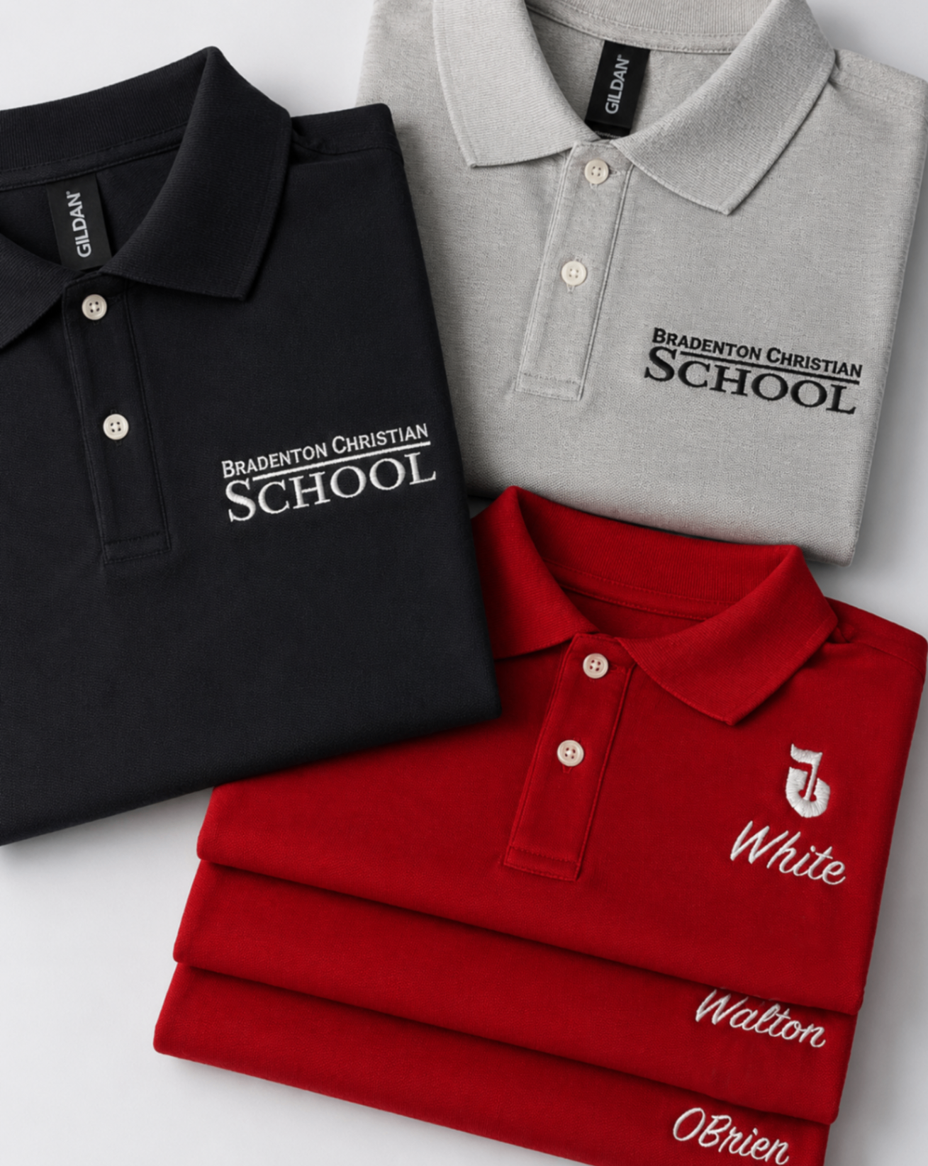 Folded black, gray, and red Bradenton Christian School polos with embroidered logos and personalized names.